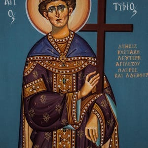 May include: An icon depicting a figure with a halo, wearing a crown and ornate robes in shades of purple, gold, and blue. The figure holds a brown cross. Greek text is visible in the background.