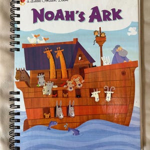 May include: A spiral-bound children's book titled "Noah's Ark" with colorful illustrations. The cover features a depiction of Noah's Ark with various animals, including giraffes, lions, and ducks, set against a blue sky and water background.