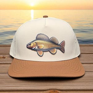 May include: A beige and brown baseball cap featuring a detailed illustration of a fish. The fish is primarily gold and brown with red accents. The cap has a curved brim and a button on top, perfect for fishing enthusiasts.