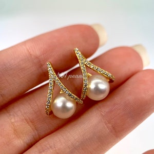 May include: Gold earrings with a V-shaped design and a pearl drop. The earrings are set with small clear stones.
