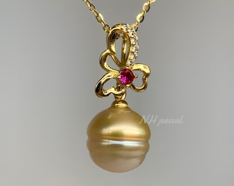 Könnte beinhalten: Eine goldene Halskette mit einem goldenen Perlenanhänger und einem Schmetterlingsanhänger mit einem roten Edelstein. Der Schmetterlingsanhänger ist mit kleinen klaren Edelsteinen verziert.