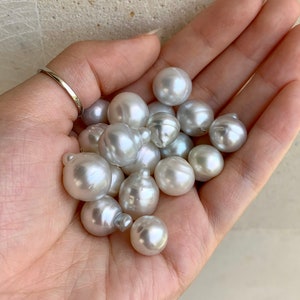 May include: A collection of white and off-white pearls of various sizes, some with a slight iridescent sheen, held in a hand.