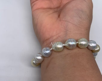 May include: A bracelet made of large, round, white and gold pearls strung on a white cord. The bracelet is worn on a person's wrist.