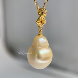 Puede incluir: Un collar con un colgante de perla barroca blanca, una cadena de oro y un engaste de oro con peque&ntilde;as piedras transparentes. La perla es grande y tiene una forma irregular.