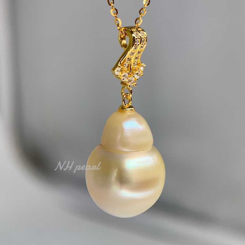 Puede incluir: Un collar con un colgante de perla barroca blanca, una cadena de oro y un engaste de oro con peque&ntilde;as piedras transparentes. La perla es grande y tiene una forma irregular.