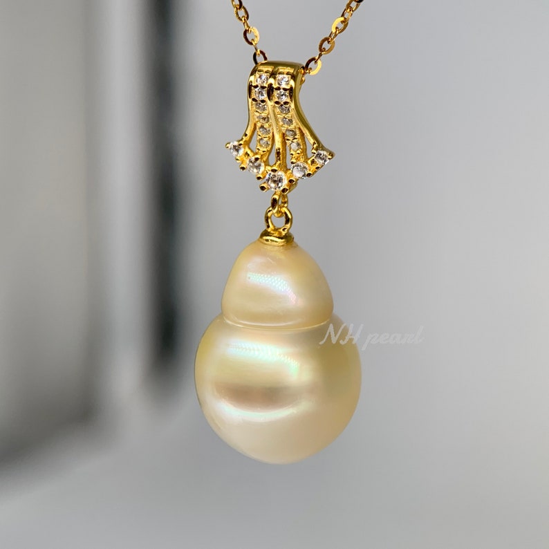 Puede incluir: Un collar de oro con un gran colgante de perla barroca blanca nacarada. El colgante est&aacute; unido a una delicada cadena de oro con un peque&ntilde;o dise&ntilde;o ornamentado de oro y cristal.