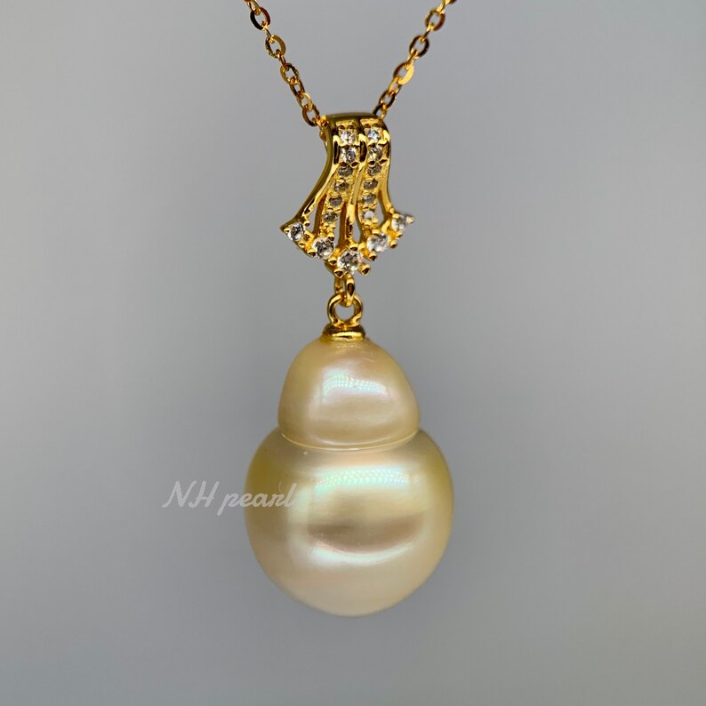 Puede incluir: Un collar de oro con un gran colgante de perla barroca blanca nacarada. El colgante est&aacute; unido a una delicada cadena de oro con un peque&ntilde;o colgante en forma de diamante.