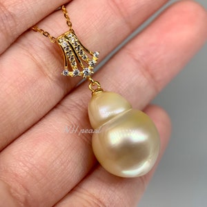 Puede incluir: Un collar con un colgante de oro adornado con una gran perla blanca nacarada del mar del Sur. La perla tiene forma de calabaza y cuelga de una delicada cadena dorada con un peque&ntilde;o colgante en forma de diamante.