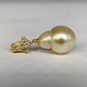 Puede incluir: Un colgante de perla barroca grande, de color blanco roto, con engaste de oro y piedras de circonita c&uacute;bica transparentes. La perla tiene un ligero brillo iridiscente.