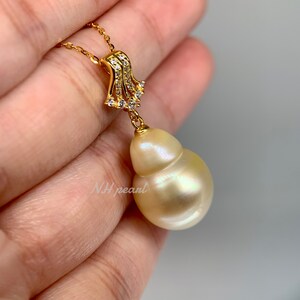 Puede incluir: Un collar de oro con un colgante de perla barroca. La perla es de color crema claro y tiene una forma &uacute;nica. El colgante est&aacute; engastado con peque&ntilde;as piedras transparentes.