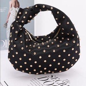 May include: A black handbag with gold studs. The bag has a knotted handle and a zipper closure.