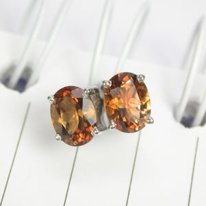 May include: A pair of silver stud earrings with oval-shaped brown gemstones.