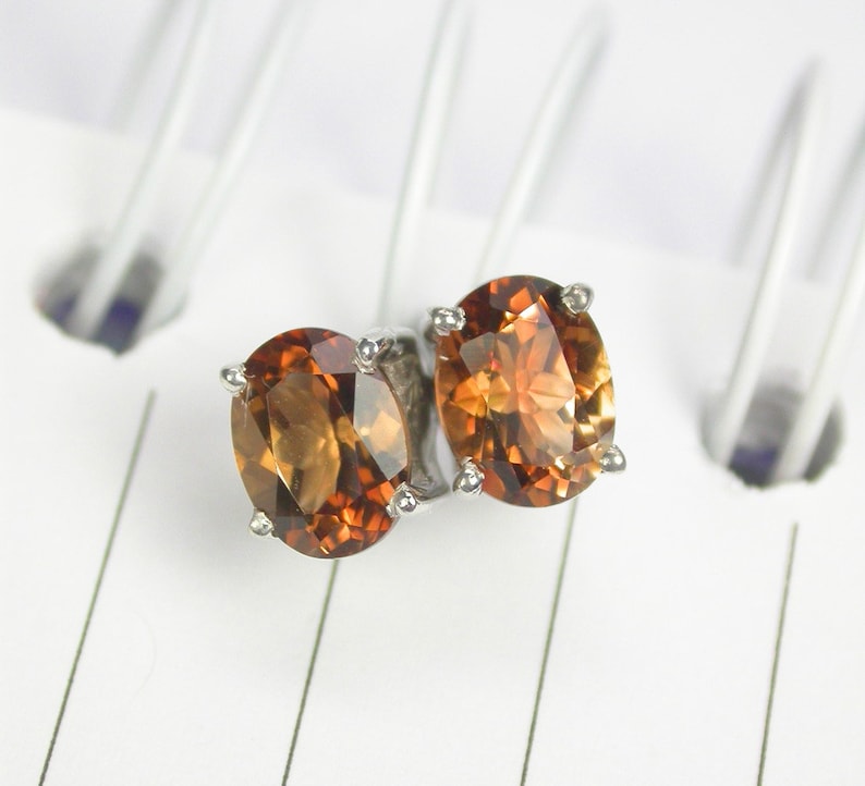 May include: A pair of silver stud earrings with oval-shaped brown gemstones.