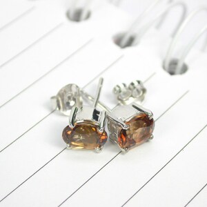 May include: A pair of silver stud earrings with oval-shaped brown gemstones.