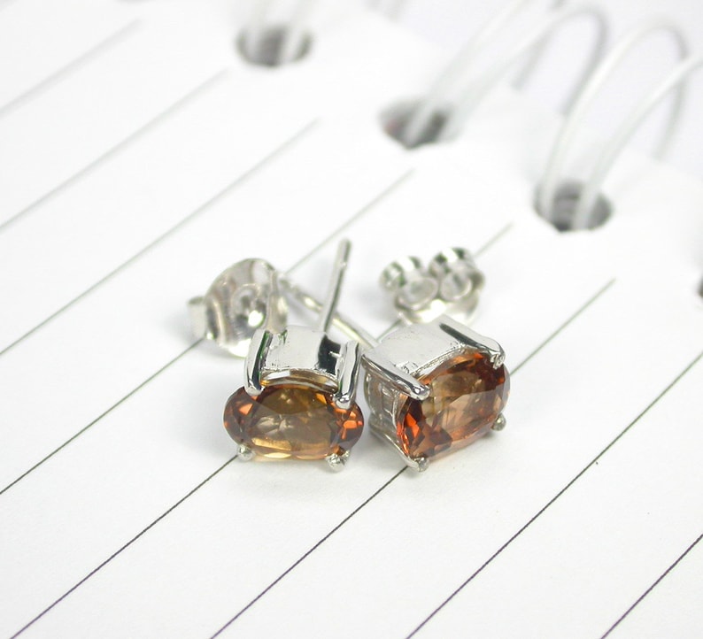 May include: A pair of silver stud earrings with oval-shaped brown gemstones.