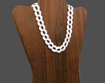 May include: A white chain necklace displayed on a wooden jewelry bust. The necklace is composed of interlocking oval links. The bust is a dark brown color, and the background is a solid gray.