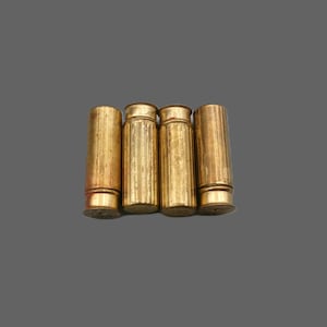 May include: Four cylindrical brass casings arranged side by side. Each casing features a metallic gold finish with vertical ribbed textures along the body and a distinct rimmed base. The metal surfaces show signs of wear and aged patina.