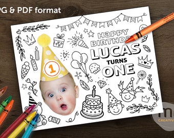 May include: A black and white birthday coloring page with the text "HAPPY BIRTHDAY LUCAS TURNS ONE". The page includes illustrations of a birthday cake, balloons, and party hats. A baby wearing a party hat is in the center. An orange crayon is on the page.
