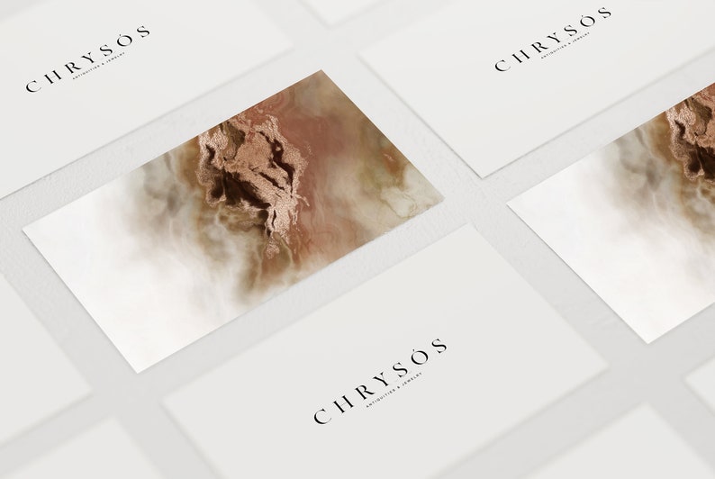 以下が含まれることがあります： 黒い文字で「CHRYSO'S ANTIQUITIES & JEWELRY」のロゴが入った白い名刺。1枚の名刺には、茶色と白の抽象的なデザインのクローズアップが施されています。名刺は白い表面に配置されています。