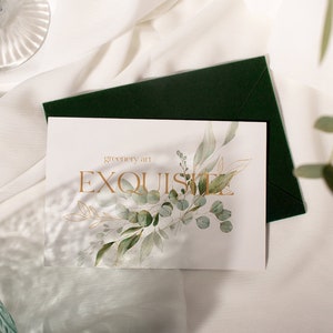 May include: A white card with the text "greenery art EXQUISITE" in gold lettering. The card is decorated with a watercolor illustration of green leaves and branches.