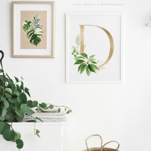 Puede incluir: Dos impresiones enmarcadas con fondo blanco. La impresi&oacute;n de la izquierda presenta una hoja tropical verde y blanca. La impresi&oacute;n de la derecha presenta una letra D dorada rodeada de hojas tropicales verdes. El texto "ARTFUL TROPICAL BOTANICALS LUSH, EXOTIC & SPONTANEOUS" est&aacute; en la parte superior de la imagen.