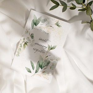 May include: A white card with a watercolor illustration of green leaves and gold accents. The text "sweet greenery exquisite" is written in black cursive on the card.