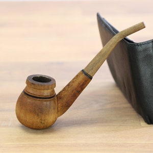 May include: A wooden pipe with a brown finish and a black leather wallet on a wooden surface.