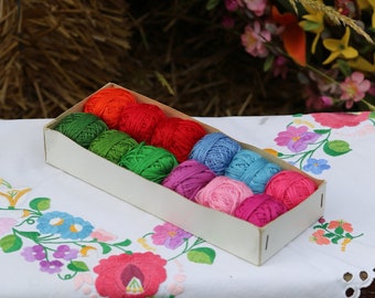 May include: A white box filled with colorful embroidery floss spools. The box is sitting on a white tablecloth with embroidered flowers.