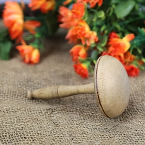 Pode incluir: Um rolo de massa de madeira com uma cabeça redonda e plana. O rolo é de cor castanho claro e tem uma borda castanho escuro em torno da cabeça. O rolo está sobre uma superfície de juta.