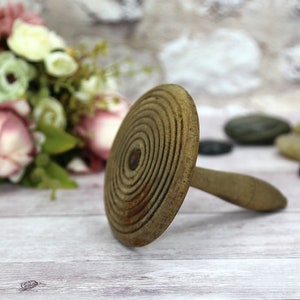 Op de afbeelding: Een houten bakgereedschap met een ronde bovenkant en een handvat. De bovenkant is versierd met concentrische cirkels. Het gereedschap ligt op een licht houten oppervlak.