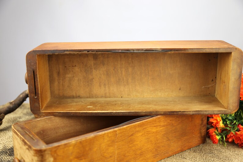 Peut inclure: Une bo&icirc;te en bois avec un couvercle &agrave; charni&egrave;re. La bo&icirc;te est en bois brun clair et a une forme rectangulaire simple. La bo&icirc;te est ouverte et vide.