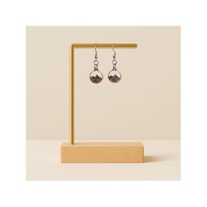 May include: Silver-toned dangle earrings with a mountain scene and the text "Mark 11:23" on a light brown background. The earrings are displayed on a gold-colored earring stand with a wooden base.