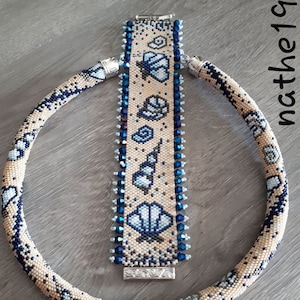 May include: A beaded necklace and bracelet set. The necklace and bracelet are beige with a blue seashell pattern. The bracelet has a rectangular shape with a silver clasp. The necklace is a circular tube shape.