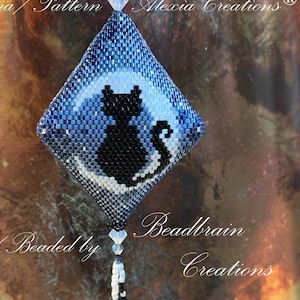 Peut inclure: Un chat noir en perles assis sur une lune croissante, sur un fond bleu et blanc. Le travail de perles est en forme de diamant et pend à une chaîne de perles.