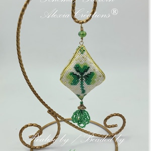 Könnte beinhalten: Ein grüner Kleeblatt-Perlen-Anhänger mit goldenen Akzenten, der an einem goldenen Metallständer hängt. Der Anhänger ist mit "Schema/Pattern Alexia Creations (R)" beschriftet.