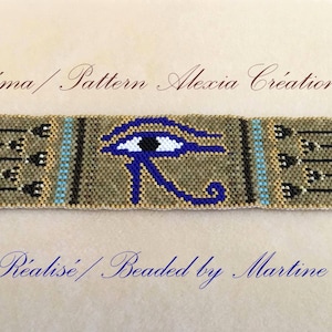 Puede incluir: Pulsera de cuentas con un diseño del Ojo de Horus en azul, negro y celeste sobre un fondo beige. La pulsera tiene extremos metálicos dorados y un cierre de cadena. El texto en la imagen dice "Schema / Pattern Alexia Creations" y "Réalisé / Beaded by Martine."