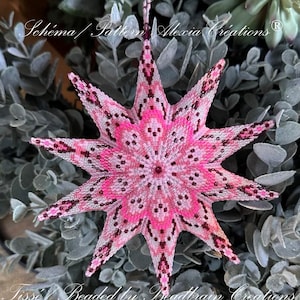 Peut inclure: Une étoile de Noël en perles rose et blanche avec un design détaillé. L'étoile est faite de petites perles et a un effet 3D. L'ornement est suspendu à une plante verte.