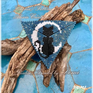 May include: A blue, black and white beaded triangle with a crescent moon design. The text "Schema/Pattern Alexia Creations (R)" and "Realise/Beaded by Domi" are visible in the image.
