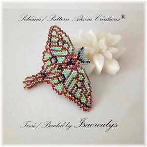 Peut inclure: Un papillon perlé avec des ailes vertes, rouges et blanches. Le papillon est posé sur une surface blanche. Le texte "Schema/Pattern Alexia Creations®" est en haut de l'image. Le texte "Tisse/Beaded by Isacrelys" est en bas de l'image.