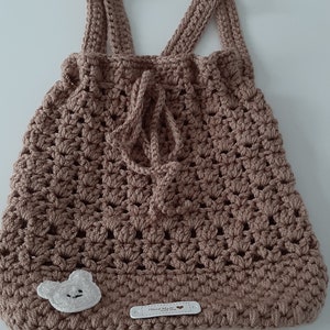 May include: A brown crocheted bag with a white bear applique and a white label that says "Hand Made" with a heart symbol.