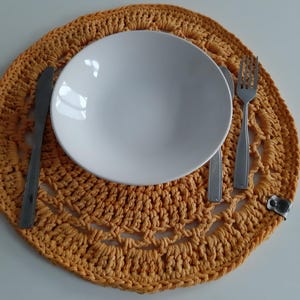 May include: A crocheted placemat in a mustard yellow color with a white plate and silverware on top.