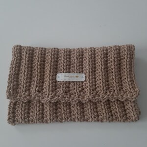 May include: A beige crocheted clutch with a scalloped edge and a small label that reads "Hand Made with Love".