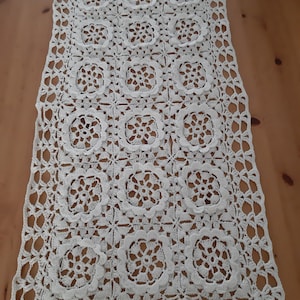 May include: White crocheted table runner with a square pattern and a delicate floral design.