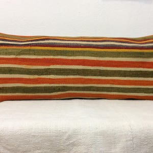 May include: A long, rectangular pillow with a striped pattern in shades of orange, green, and beige. The pillow is made of a woven fabric and has a soft, comfortable texture.