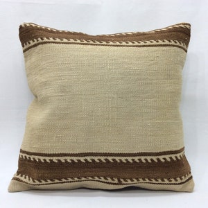 May include: A cream-coloured pillow with a brown woven border. The pillow has a simple, geometric design.
