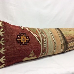 May include: A long, rectangular pillow with a red, brown, and beige patterned fabric. The pillow has a traditional Turkish design with geometric shapes and floral motifs.
