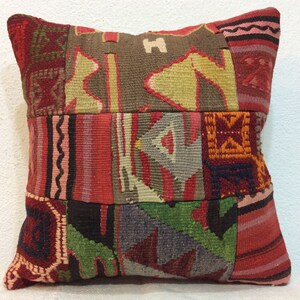 May include: A colorful patchwork pillow cover with a geometric pattern in shades of red, green, brown, and yellow. The pillow cover is made of woven fabric and has a fringed edge.