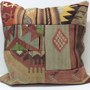 May include: A square patchwork pillow with a colorful geometric pattern in shades of red, brown, green, and blue. The pillow is made of woven fabric and has a fringed edge.