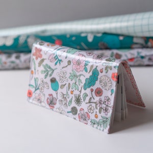 Peut inclure: Un portefeuille à motifs floraux sur fond gris clair. Le motif répété comprend des fleurs, des feuilles et des éléments botaniques en rose, turquoise et orange. Le portefeuille est ouvert, révélant l'intérieur.