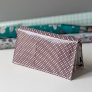May include: A brown wallet with white polka dots. The wallet is closed and has a flap that folds over the front.